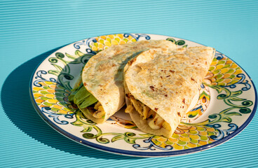 Delicious traditional quesadillas with chicken and spinach inside, on a handmade plate on a blue table.