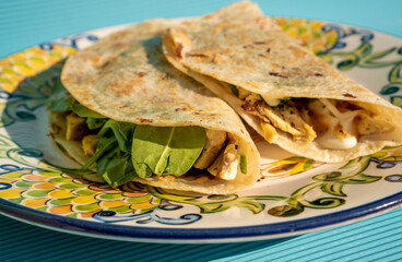 Exquisite traditional quesadillas with chicken and spinach inside, on a plate on a blue table in...