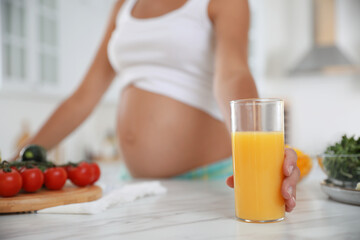 Obraz na płótnie Canvas Young pregnant woman with glass of juice at table in kitchen, closeup. Taking care of baby health