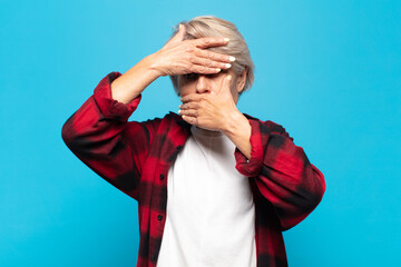 middle age woman covering face with both hands saying no to the camera! refusing pictures or...