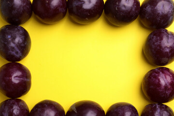Frame made of delicious ripe plums on yellow background, flat lay. Space for text
