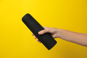 Woman holding modern black thermos on yellow background, closeup