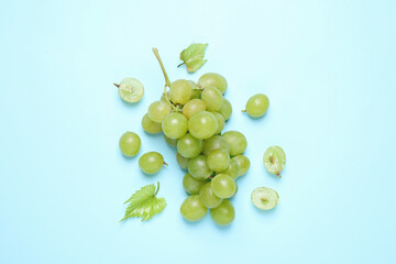 Fototapeta premium Bunch of ripe grapes with green leaves on light blue background, flat lay