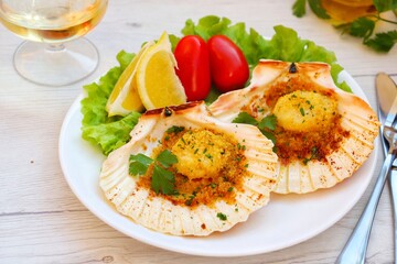 Scallops au gratin on white plate with white wood table background