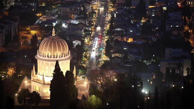 The golden dome of the Bahai Temple in Haifa illuminated by night lights. .Cars are going through the city at night.
