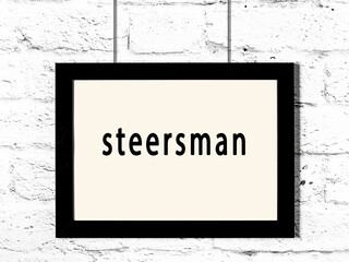 Black frame hanging on white brick wall with inscription steersman