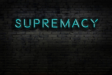 Night view of neon sign on brick wall with inscription supremacy
