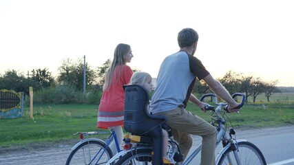 Young couple on a bike with their little daughter at sunset.