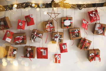 Handmade Advent calendar with gifts hanging on white wall. Christmas season