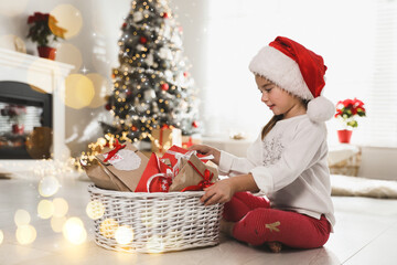 Cute little girl in Santa hat taking gift from Christmas advent calendar at home. Bokeh effect