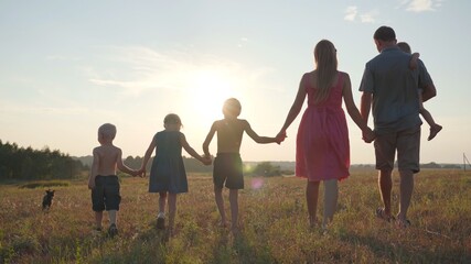 A friendly large family walks across the field at sunset with dog.