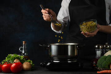 Professional chef pours canned greens peas into pan for cooking soup on dark blue background....