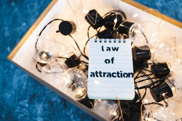 law of attraction and positive mindset, box as metaphor of the mind with Law Of Attraction notepad on top of plenty of idea light bulbs surrounded by fairy lights