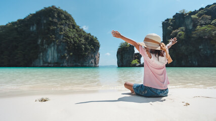 Backside of asian child girl wearing hat sitting on the beach and enjoying with beautiful nature in her vacation with family. Family trip and Thailand travel concept.