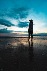 Silhouette of young asian woman standing on the beach and looking at beautiful sea and sky at the sunset time.