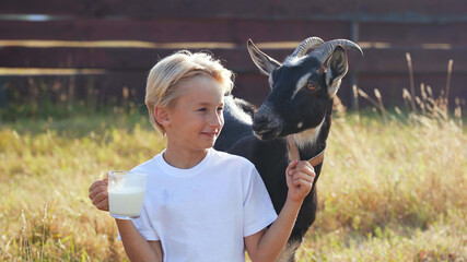 A boy drinks goat milk from a mug next to his goat. - Powered by Adobe