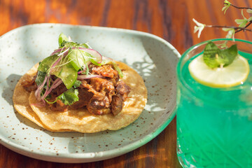 Gourmet Mexican shredded meat tacos and green cocktail on wooden table.