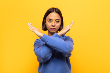 young latin woman looking annoyed and sick of your attitude, saying enough! hands crossed up front,...