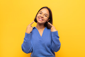 young latin woman smiling confidently pointing to own broad smile, positive, relaxed, satisfied...