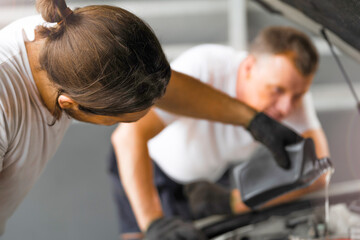 worker men repairing is pouring Motor oil in engine vehicle at petrol pump garage repairing center....