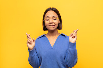 young latin woman smiling and anxiously crossing both fingers, feeling worried and wishing or...