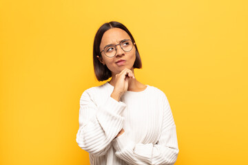 young latin woman feeling thoughtful, wondering or imagining ideas, daydreaming and looking up to...