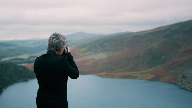 Woman standing on a hill by the lake and taking pictures