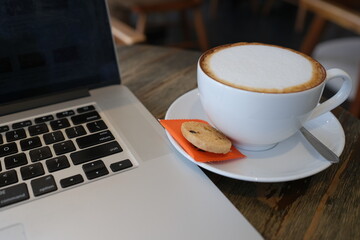 A cup of cappuccino coffee or latte coffee in a white cup with laptop on table. Royalty high quality free stock photo of drink capuccino or latte coffe with laptop for working in office