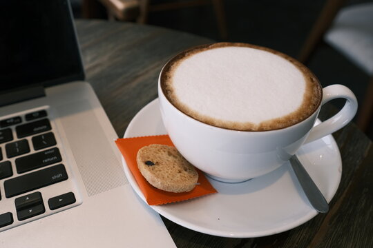 A cup of cappuccino coffee or latte coffee in a white cup with laptop on table. Royalty high quality free stock photo of drink capuccino or latte coffe with laptop for working in office