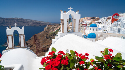 Naklejka premium Blue domed church in Oia, Santorini with bougainvillea flowers on th foreground