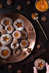 Top down vertical view of chocolate Linzer cookies on a copper tray with a hand holding one cookie.