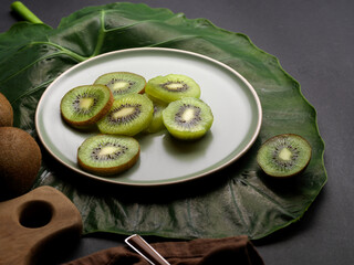 Sliced fresh kiwi fruit on plate decorated with green leaf on kitchen table