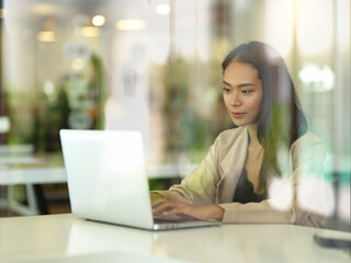 Obraz na płótnie Canvas View through glass wall of female working with laptop
