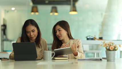 Two female office workers working with tablet in modern meeting room