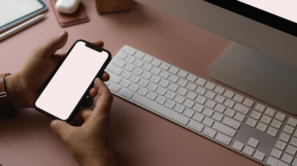 Male hands holding smartphone on worktable with computer devices
