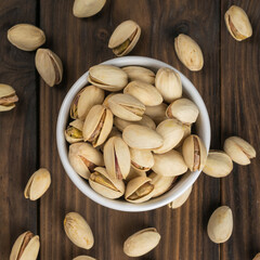 Top view of a white bowl of pistachios on a wooden table.