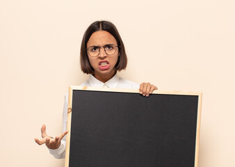 young latin woman looking angry, annoyed and frustrated screaming wtf or what’s wrong with you