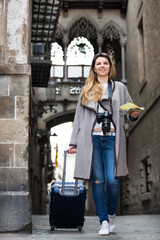 Fototapeta na wymiar Smiling young tourist blond girl taking a walk in the town streets with a travel bag