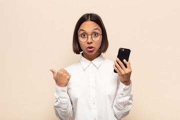 young latin woman looking astonished in disbelief, pointing at object on the side and saying wow,...