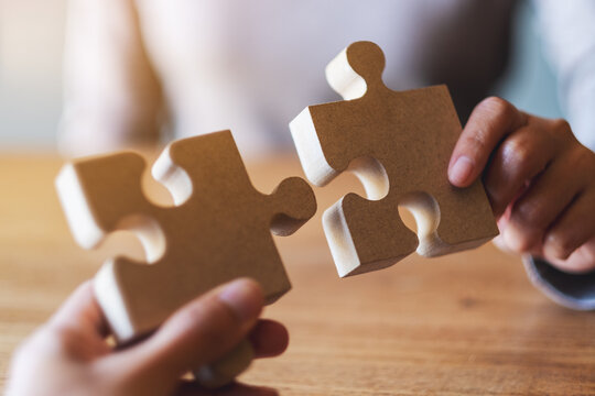 Closeup image of two people holding and putting a piece of wooden jigsaw puzzle together
