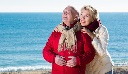 Fototapeta na wymiar Aged husband and wife taking stroll on beach and watching skies