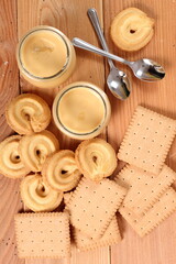 Milk pudding dessert in jar and cookies at wooden plank background. Directly Above.