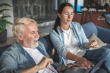 Daughter teaches her adult dad pensioner to use payment card on Internet on laptop