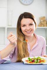 Young smiling girl enjoying tasty green salad at home.