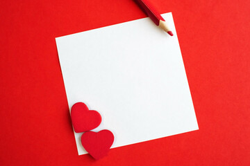 a white square sheet of paper with a red heart and pencil on a red background. Holiday background with space for text.