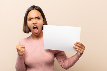 young latin woman shouting aggressively with an angry expression or with fists clenched celebrating...