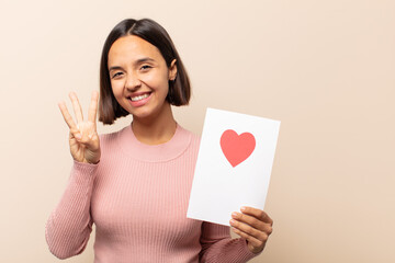 young latin woman smiling and looking friendly, showing number three or third with hand forward,...