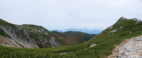 Naklejka na ściany i meble Panorama view of grassy mountain range and cloudy blue horizon in early autumn at Senjojiki Cirque in Nagano Prefecture, Japan.