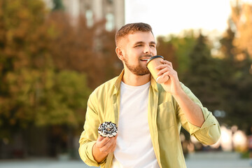 Handsome young man with sweet donut and coffee outdoors