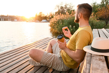 Handsome young man with sweet donut and coffee near river